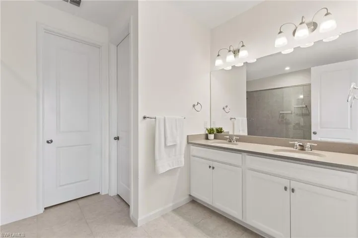 Bathroom featuring double vanity, light tile patterned floors, and a tile shower