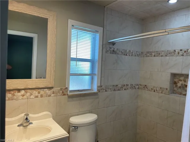 Bathroom featuring vanity, tile walls, tiled shower, and a wainscoted wall