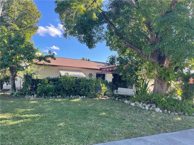 View of property hidden behind natural elements featuring stucco siding and a front yard