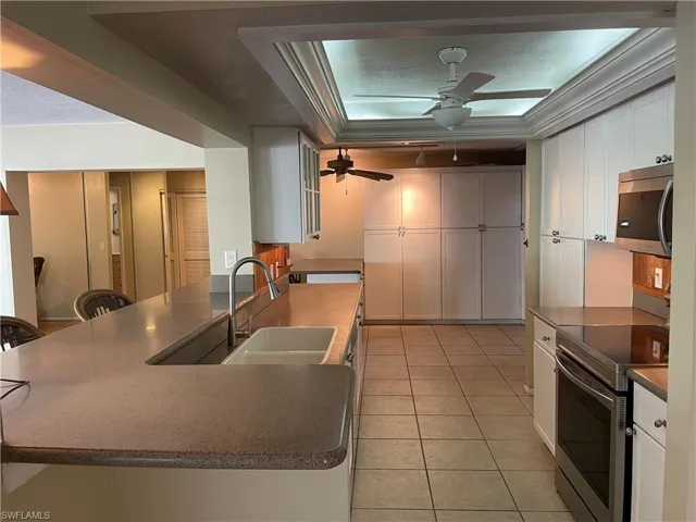 Kitchen with white cabinets, stainless steel appliances, dark countertops, light tile patterned flooring, and a peninsula