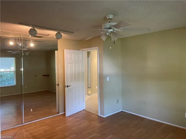 Unfurnished bedroom with a textured ceiling, a closet, wood finished floors, and a ceiling fan