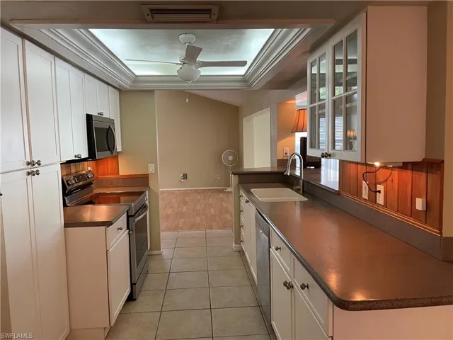 Kitchen with dark countertops, appliances with stainless steel finishes, glass insert cabinets, a ceiling fan, and a raised ceiling