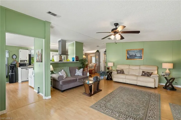 Living room with ceiling fan, a textured ceiling, and light hardwood / wood-style floors