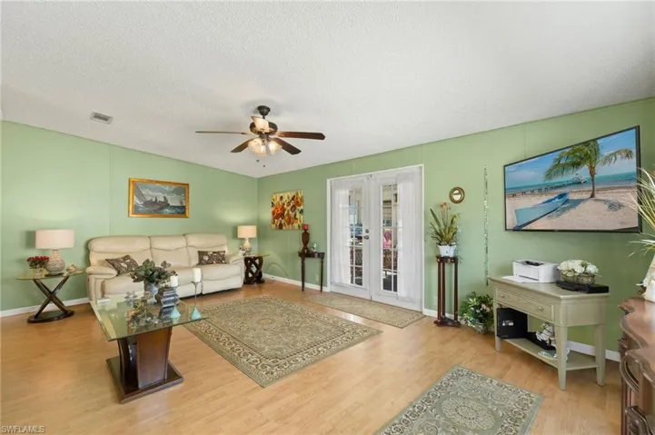 Living room with ceiling fan, french doors, a textured ceiling, and light wood-type flooring