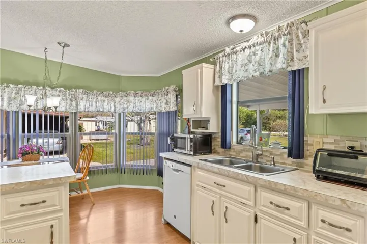 Kitchen with sink, white dishwasher, light hardwood / wood-style floors, decorative light fixtures, and a chandelier