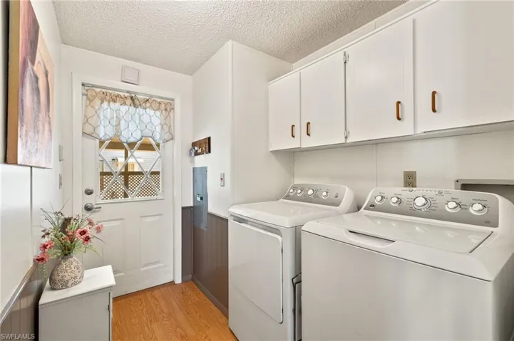 Laundry area featuring cabinets, a textured ceiling, washing machine and clothes dryer, and light hardwood / wood-style floors