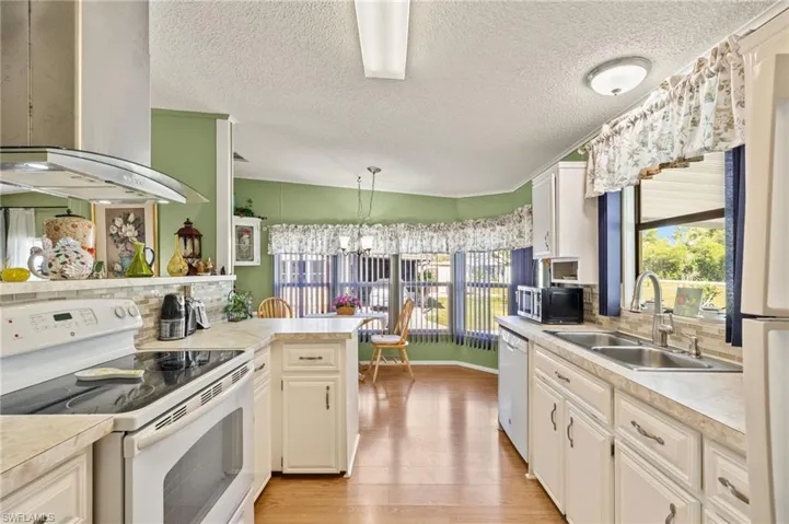 Kitchen with sink, light wood-type flooring, hanging light fixtures, island exhaust hood, and white appliances
