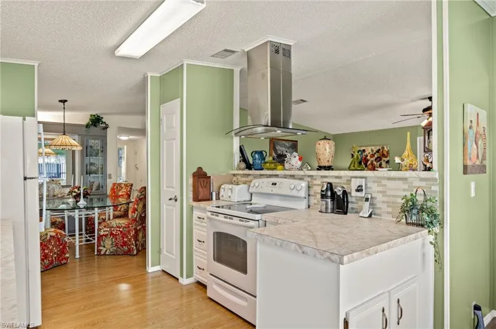 Kitchen featuring white cabinetry, island range hood, light wood-type flooring, pendant lighting, and white appliances