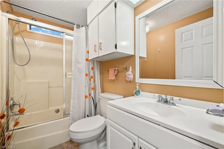 Full bathroom with toilet, vanity, shower / bathtub combination with curtain, and a textured ceiling