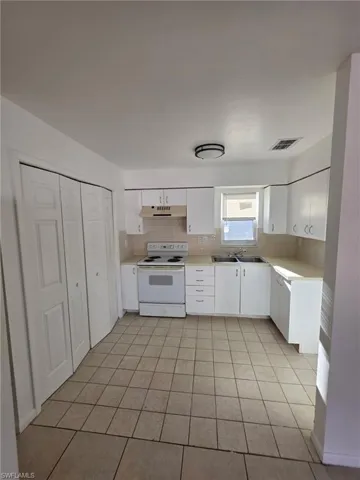 Kitchen featuring white electric stove, light countertops, white cabinetry, and backsplash