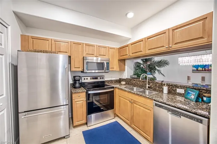 Kitchen with appliances with stainless steel finishes, sink, dark stone counters, and light tile patterned floors