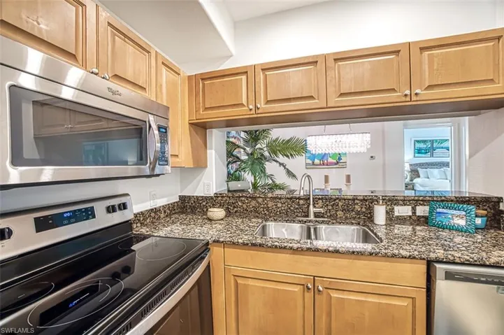 Kitchen with sink, a notable chandelier, stainless steel appliances, and dark stone countertops
