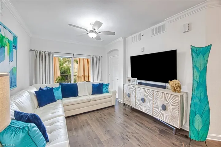 Living room with dark wood-type flooring, crown molding, and ceiling fan