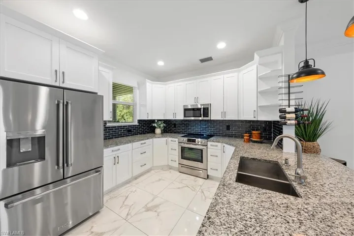 Kitchen featuring stainless steel appliances, a sink, open shelves, light marble finish floors, and white cabinetry