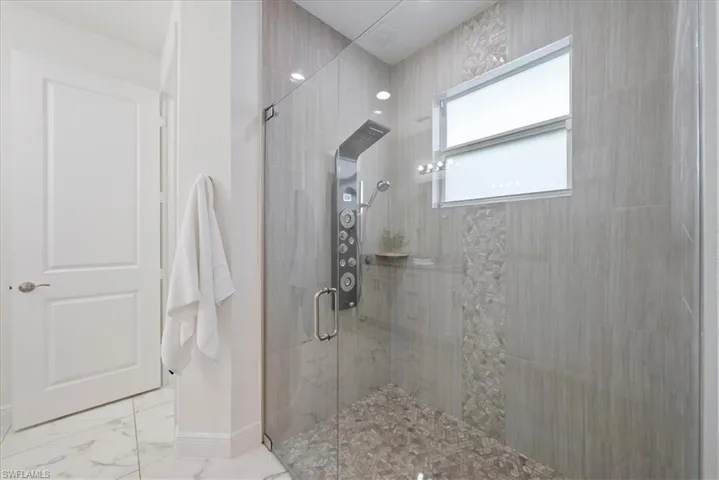 Bathroom featuring tiled shower, marble finish flooring, and baseboards