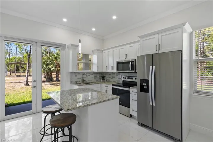 Guest home kitchen with appliances with stainless steel finishes, sink, tasteful backsplash, a center island, and light stone countertops