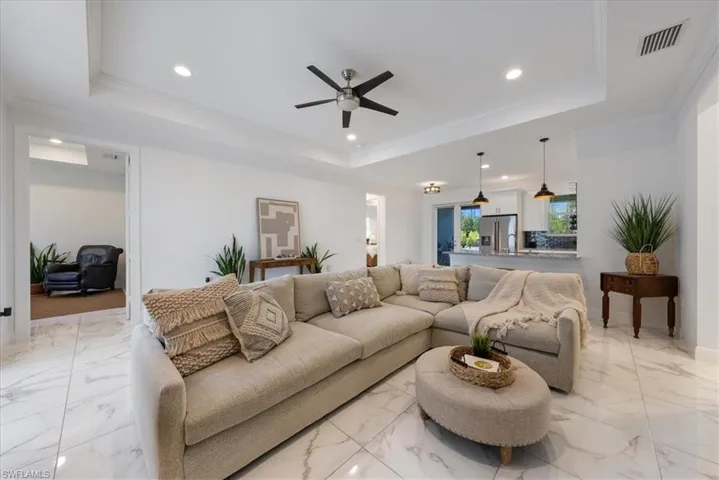 Living area featuring a raised ceiling, ceiling fan, light marble finish floors, recessed lighting, and crown molding