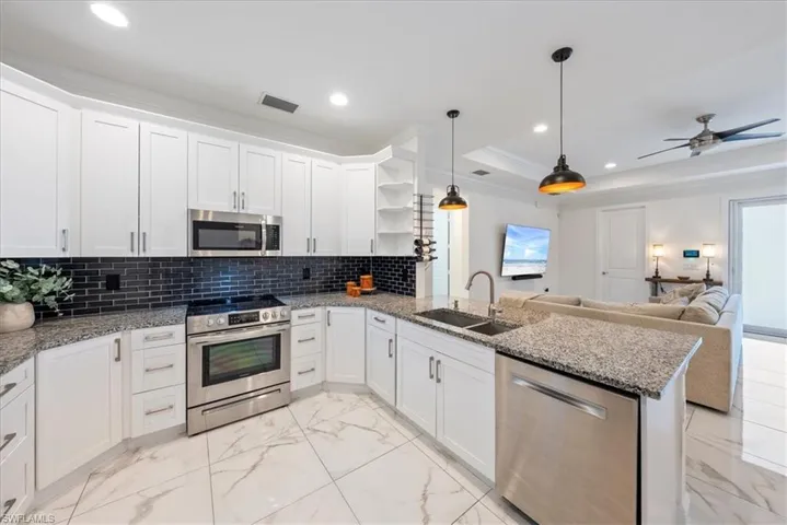 Kitchen with appliances with stainless steel finishes, a sink, open shelves, light marble finish flooring, and a peninsula