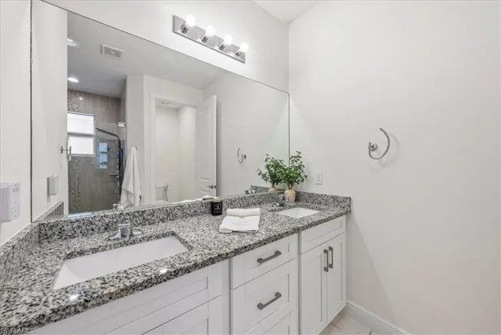 Full bathroom featuring a stall shower, double vanity, baseboards, and toilet