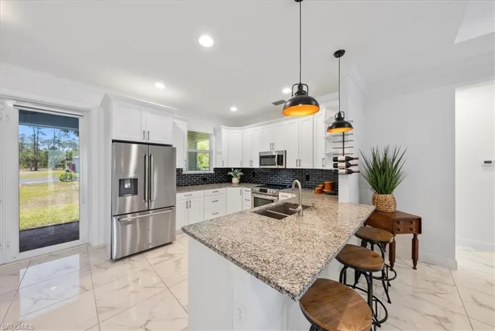 Kitchen featuring appliances with stainless steel finishes, a peninsula, light marble finish floors, a kitchen breakfast bar, and crown molding
