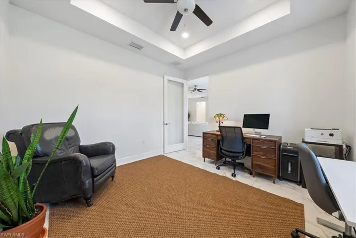 Office space featuring a ceiling fan, light marble finish floors, baseboards, a tray ceiling, and recessed lighting
