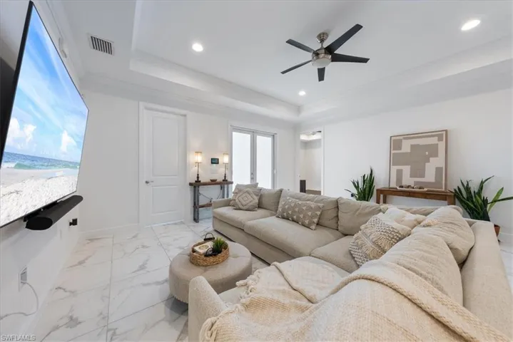 Living room with a raised ceiling, ceiling fan, recessed lighting, baseboards, and light marble finish flooring