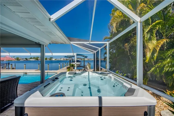 View of pool featuring a lanai, a water view, a patio area, and a hot tub
