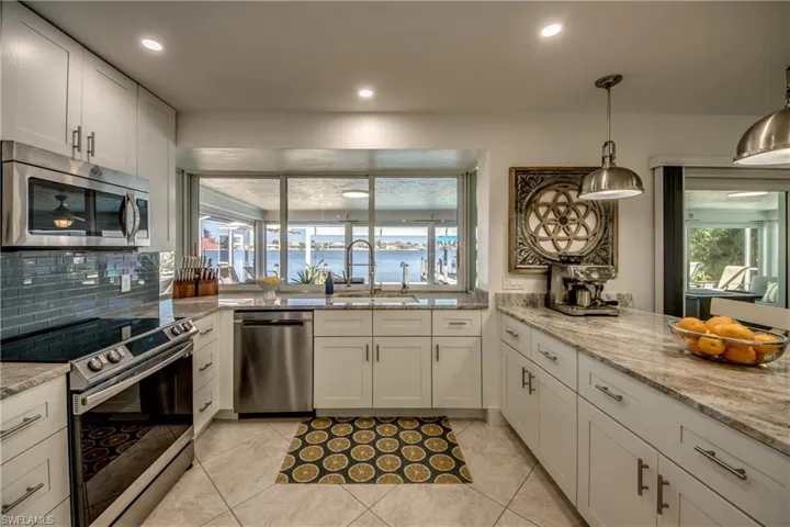Kitchen featuring light tile patterned floors, appliances with stainless steel finishes, hanging light fixtures, sink, and white cabinetry