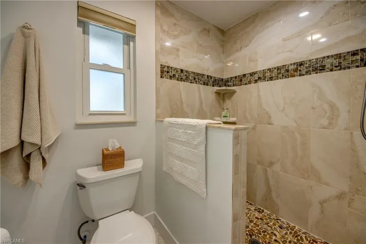 Bathroom with tiled shower, toilet, and a wealth of natural light