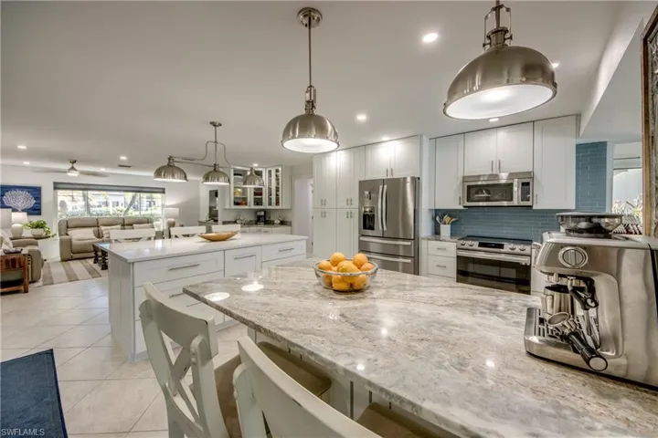 Kitchen with hanging light fixtures, appliances with stainless steel finishes, light stone counters, white cabinetry, and a kitchen breakfast bar