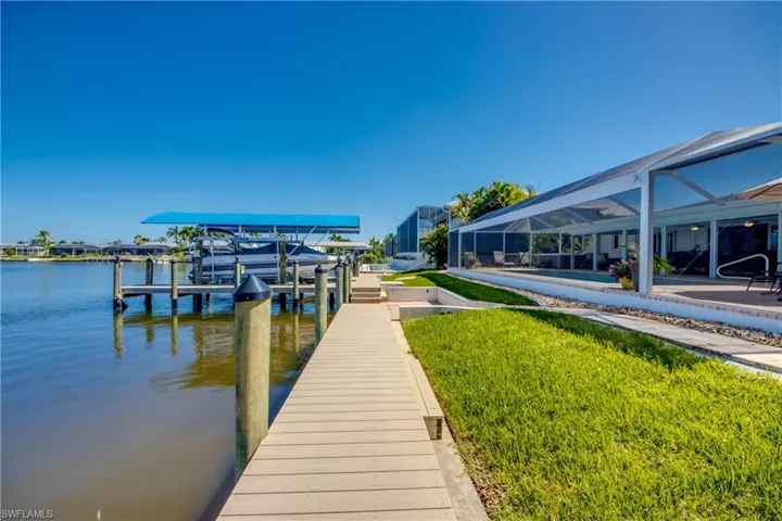 Dock area featuring glass enclosure, a lawn, and a water view