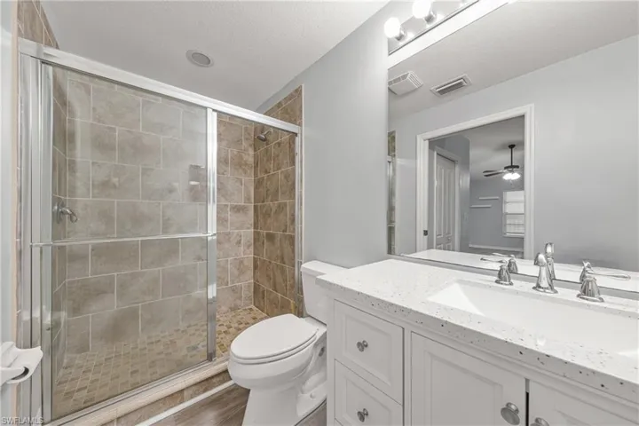 Bathroom featuring a tiled walk-in shower with glass enclosure, white vanity with integrated sink, speckled countertop, and wall-mounted mirror