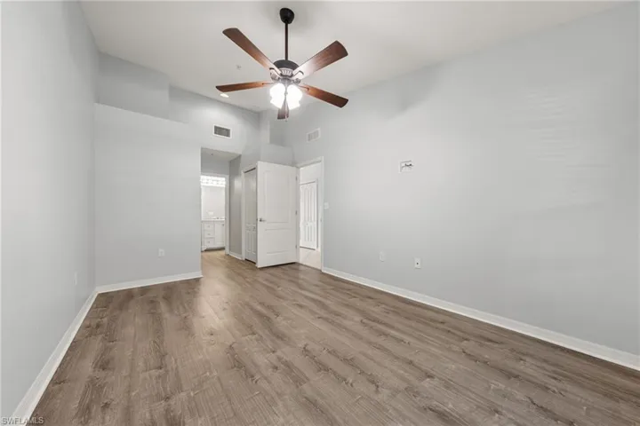 Spacious room featuring wood-finish flooring, light gray walls, and a ceiling fan with integrated lighting
