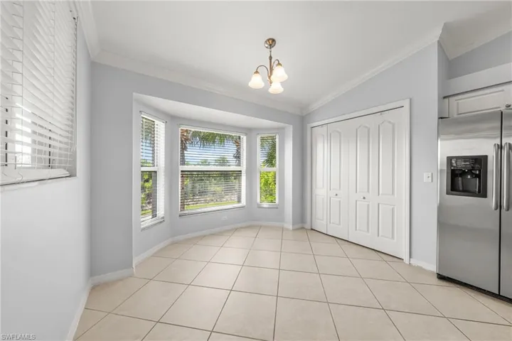 Dining area featuring a bay window, crown molding, white bi-fold closet doors, stainless steel refrigerator, and tiled flooring