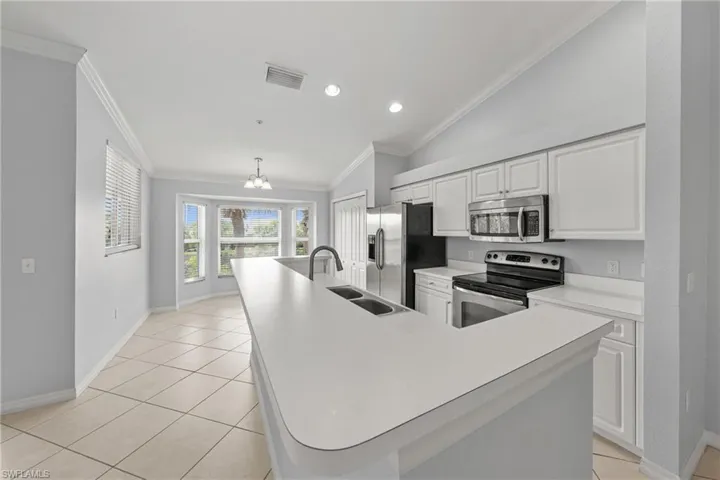 Kitchen featuring a large central island with double sink, white cabinetry, stainless steel appliances, and tile flooring