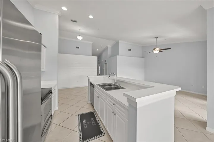 Kitchen featuring a stainless steel refrigerator, white cabinetry, a double basin sink, and a breakfast bar with white countertops