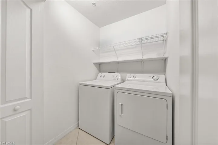 Dedicated laundry space featuring a white washer and dryer, tile flooring, and integrated wire shelving for storage
