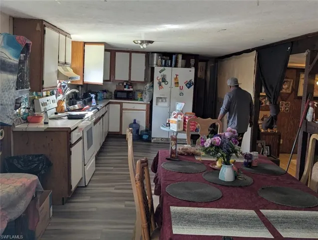 Kitchen featuring wood finished floors, white appliances, light countertops, white cabinetry, and under cabinet range hood