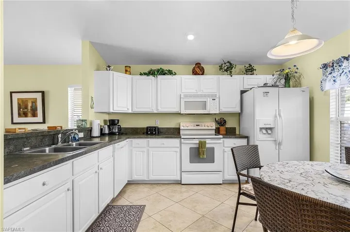 Kitchen with white appliances, dark countertops, white cabinetry, hanging light fixtures, and light tile patterned flooring