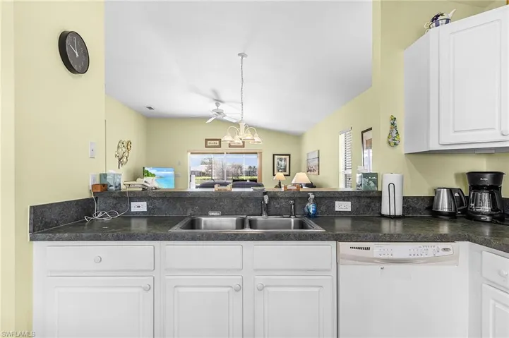 Kitchen with white cabinetry, dishwasher, hanging lights, dark countertops, and vaulted ceiling