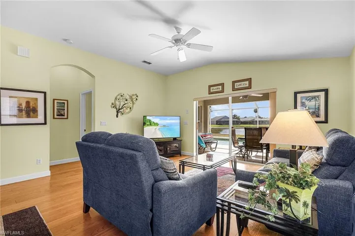 Living area featuring arched walkways, a ceiling fan, wood finished floors, and vaulted ceiling