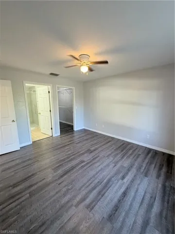 Spacious room featuring wood-finish flooring, a ceiling fan with integrated lighting, white baseboards, and neutral wall tones