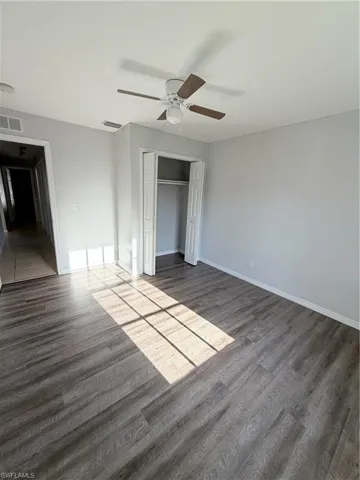 Spacious room featuring wood-finish flooring, light gray wall paint, and a ceiling fan with wood-tone blades