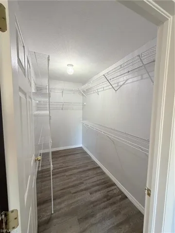 Walk-in closet featuring wood-finish flooring, white wire shelving, a ceiling light fixture, and white baseboards