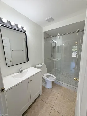 Full bathroom featuring a white vanity with integrated sink, a frameless shower enclosure with sliding glass doors, a single-handle chrome faucet, and tiled flooring