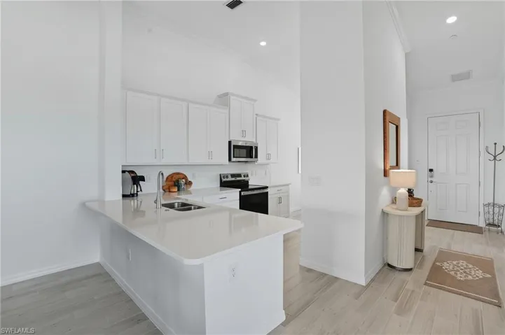 Kitchen featuring white cabinetry, stainless steel appliances, light wood finished floors, crown molding, and a peninsula