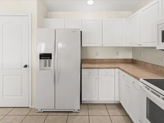 Kitchen with white appliances, white cabinetry, and light tile patterned flooring