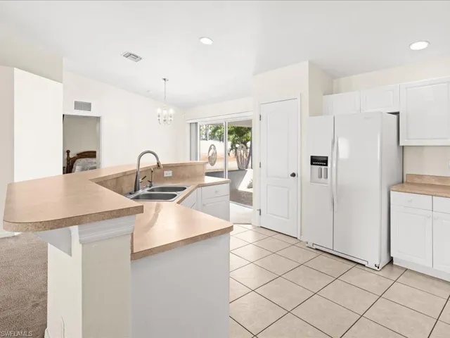 Kitchen with white refrigerator with ice dispenser, an island with sink, light countertops, light tile patterned floors, and white cabinetry