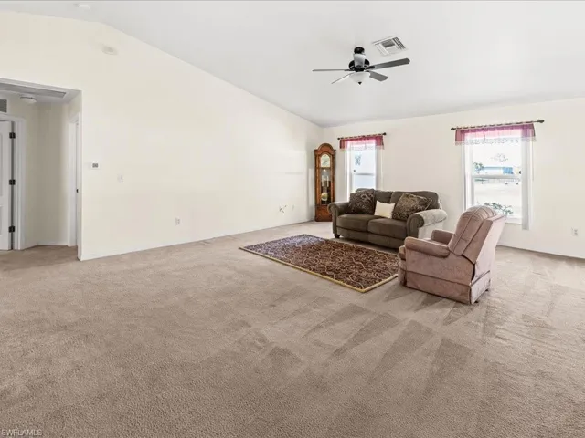 Living area with light carpet, lofted ceiling, and ceiling fan