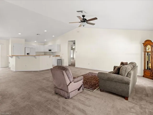 Living area with lofted ceiling, light carpet, ceiling fan, and recessed lighting